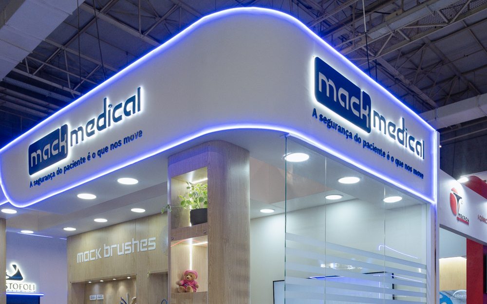 Estande da Mack Medical na SOBECC de 2025, com o logotipo iluminado na testeira e a prateleira da linha mack brushes