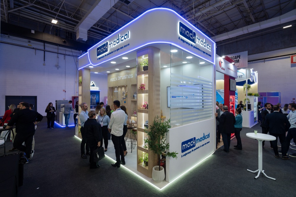 Estande da Mack Medical na SOBECC 2025, com o logotipo iluminado na testeira e a prateleira da linha mack brushes